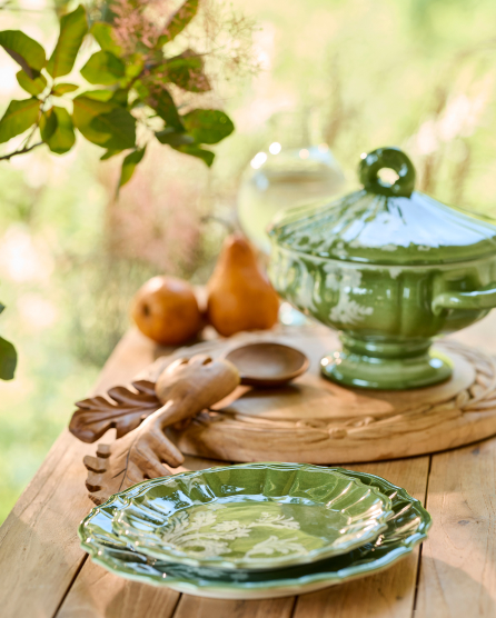 Green glass serving dishes and wooden utensils arranged on a rustic wooden table with fresh greenery and soft natural lighting.