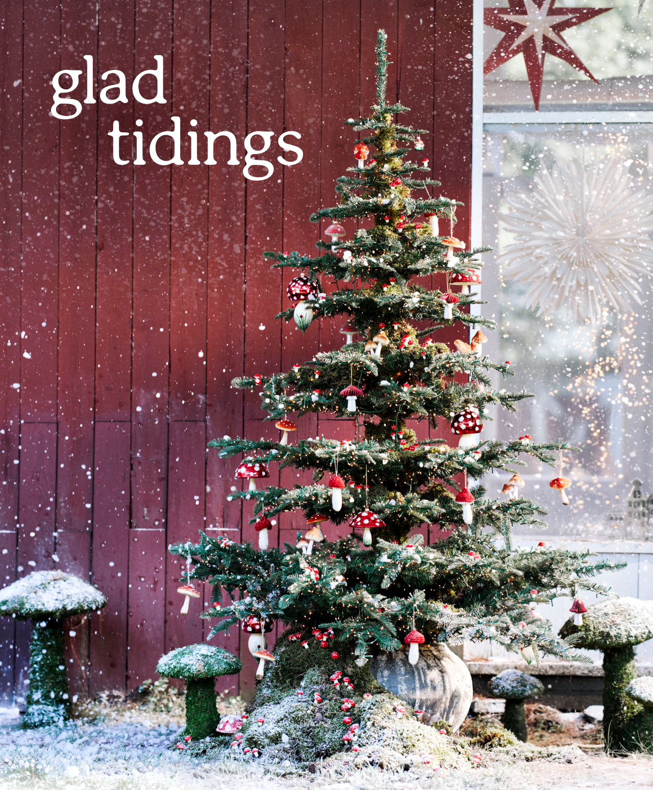 Decorated Christmas tree with falling snow beside red barn wall and window with star decorations displaying glad tidings text