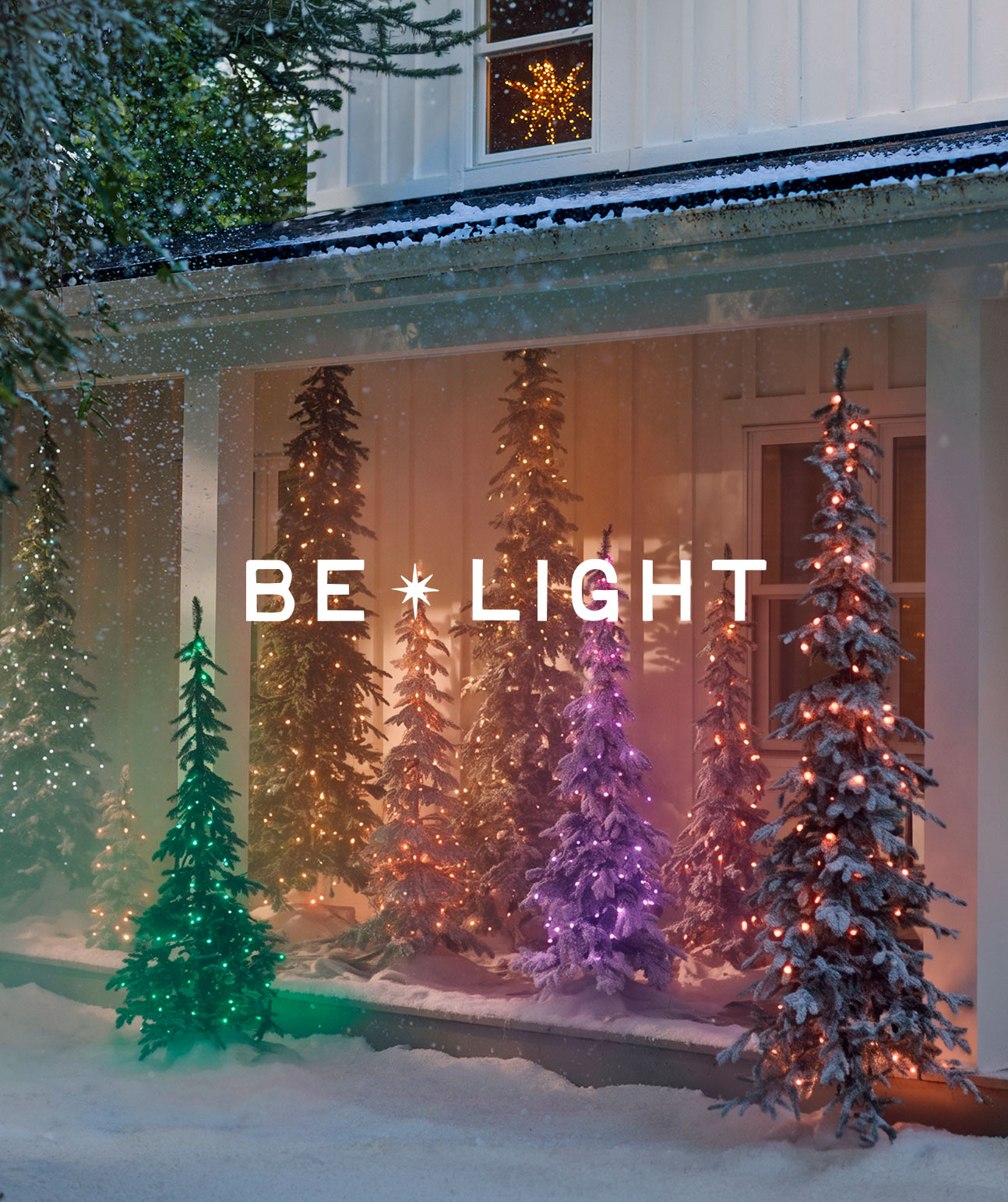 Illuminated Christmas trees in various colors on a snowy porch with BE LIGHT text overlay and star decoration in window.
