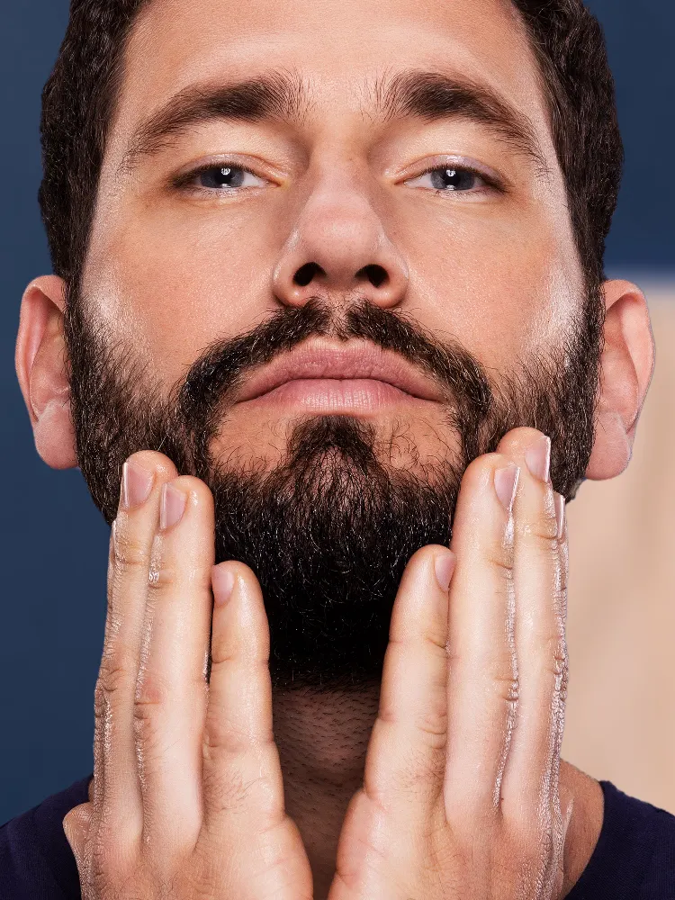 Primer plano de una persona con barba tocándola con ambas manos, mostrando el tema de la caspa en la barba.