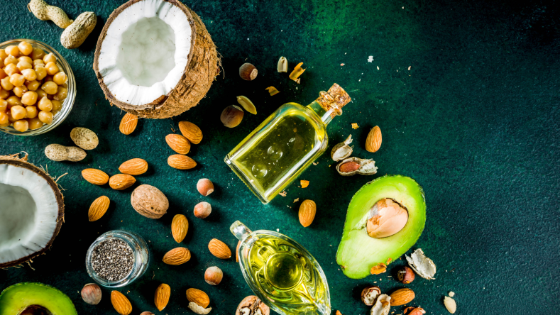Sources of fat such as olive oil, avocado, almonds and coconut on a green background