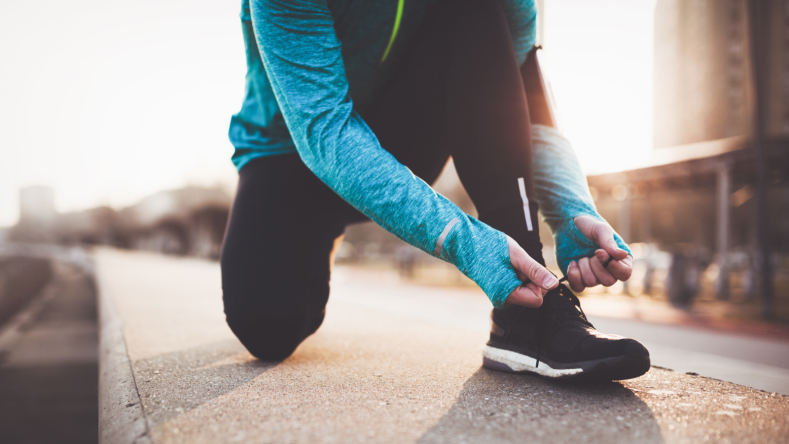 Runner in a teal top lacing up running shoes