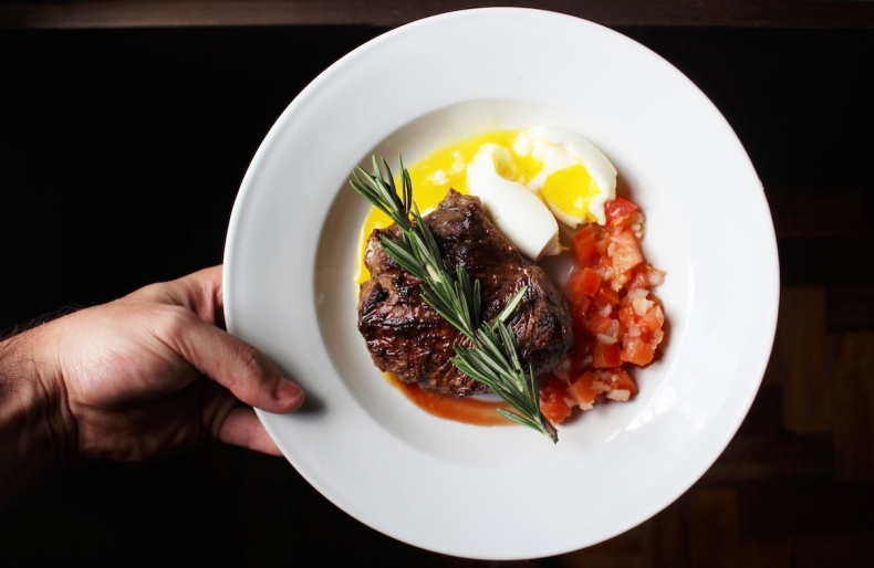 steak, egg and tomatoes on a white plate against a black background
