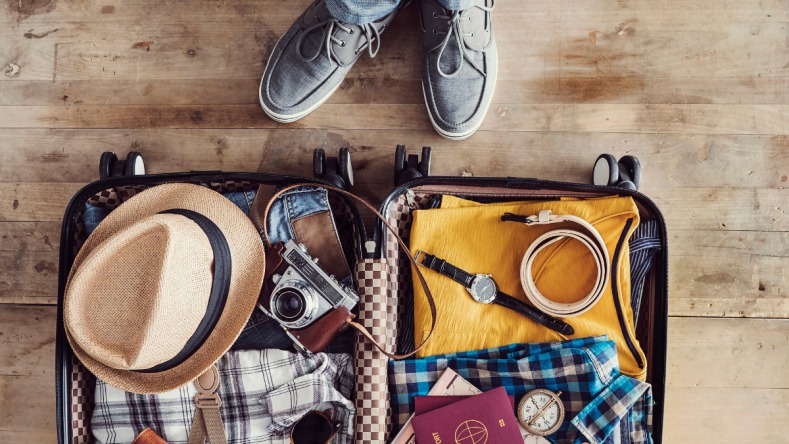Open suitcase containing clothes, passport, hat, camera, watch and belt