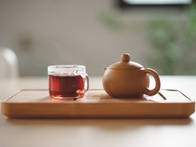 Clear cup filled with tea next to a teapot on a wooden stand