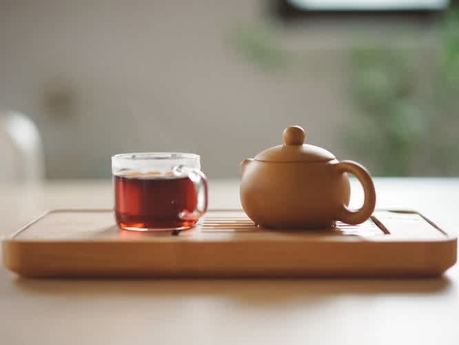 Clear cup filled with tea next to a teapot on a wooden stand