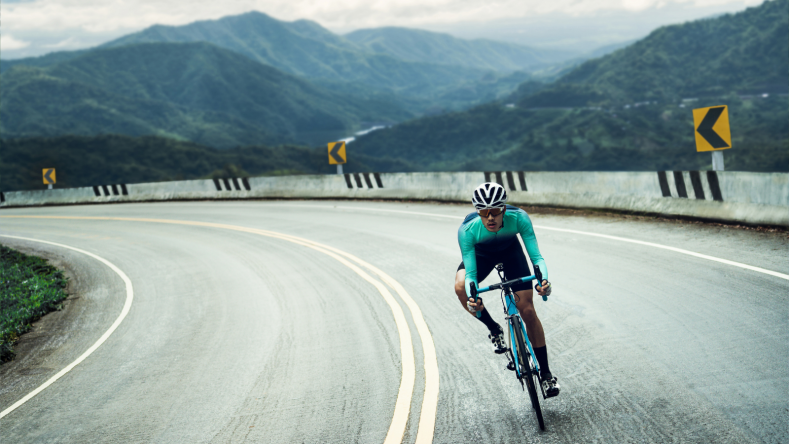 Man cycling in a teal jersey with mountains in the background