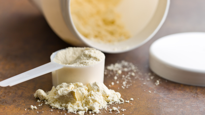 Whey protein in a clear scoop on a wooden background