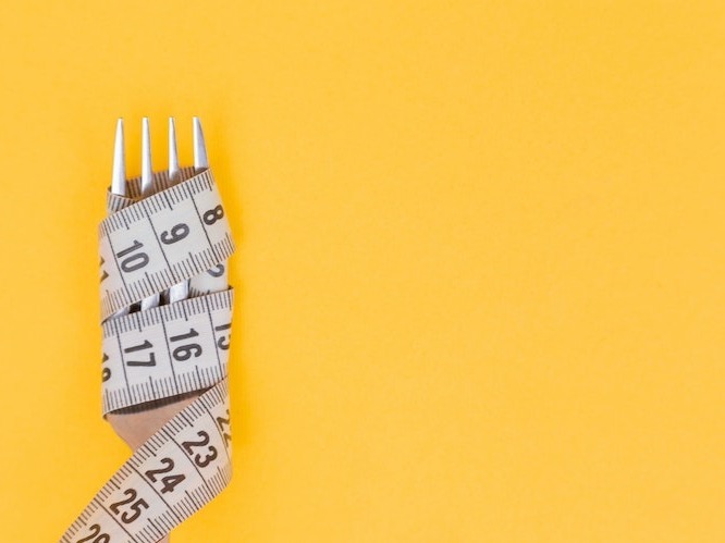 Tape measure wrapped around fork on a yellow background