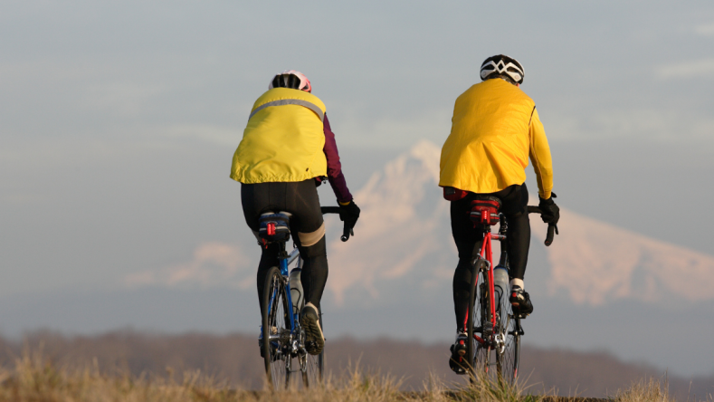 The back of two cyclists in yellow jerseys with a mountain in the background