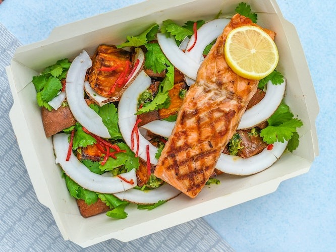 Cooked salmon on a bed of greens on a baby blue table