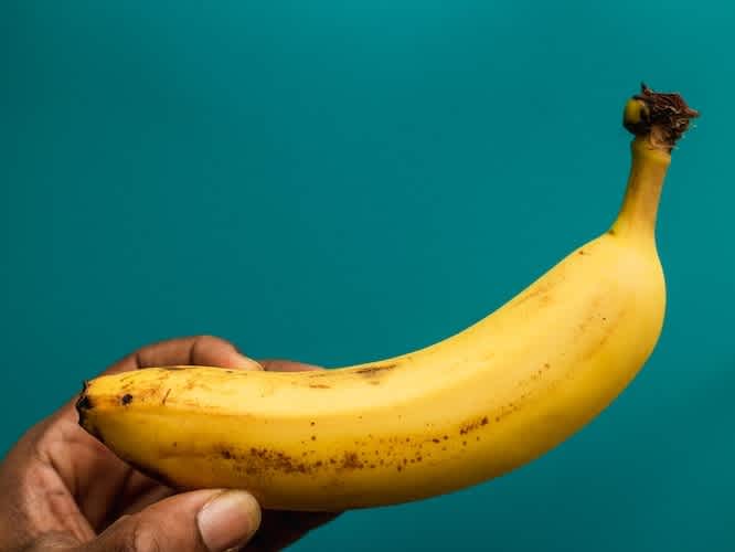 Hand holding a banana on a teal background