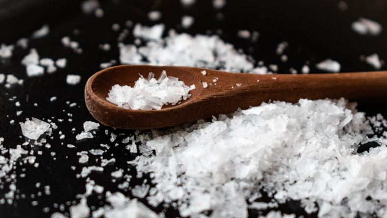 Salt on a wooden spoon on a black background