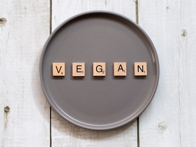 Vegan spelled out with scrabble tiles on a gray plate, on a white background