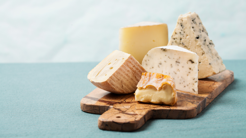 5 cheese wedges on a wooden board against a blue and gray background
