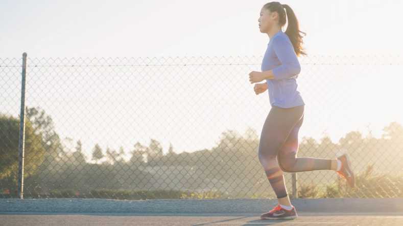 woman with ponytail running along road against a fenced background