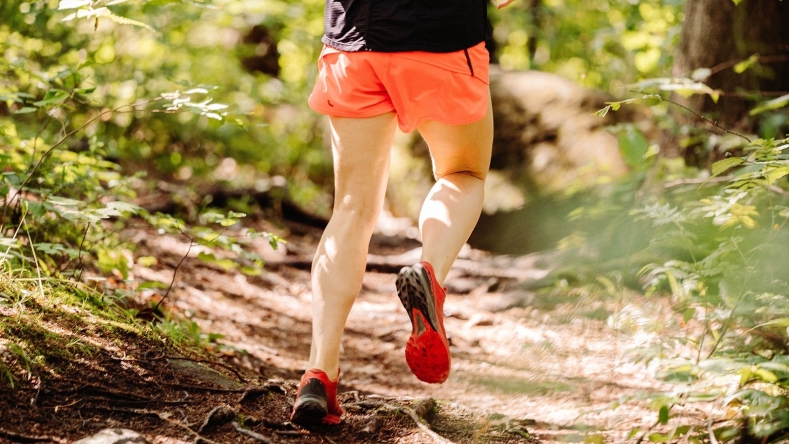 person with a black shirt and orange shorts and red sneakers running in woods