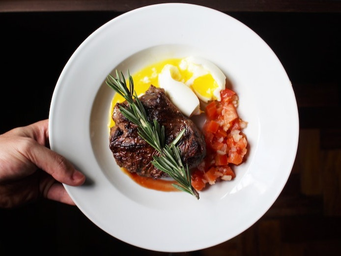 Steak served with an egg and tomatoes in a white bowl
