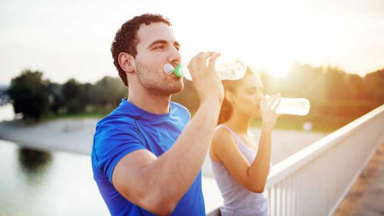 Man and woman drinking water on a bridge after exercise
