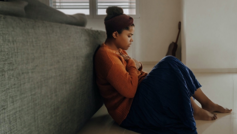 Anxious woman sitting on ground with hands on chest 