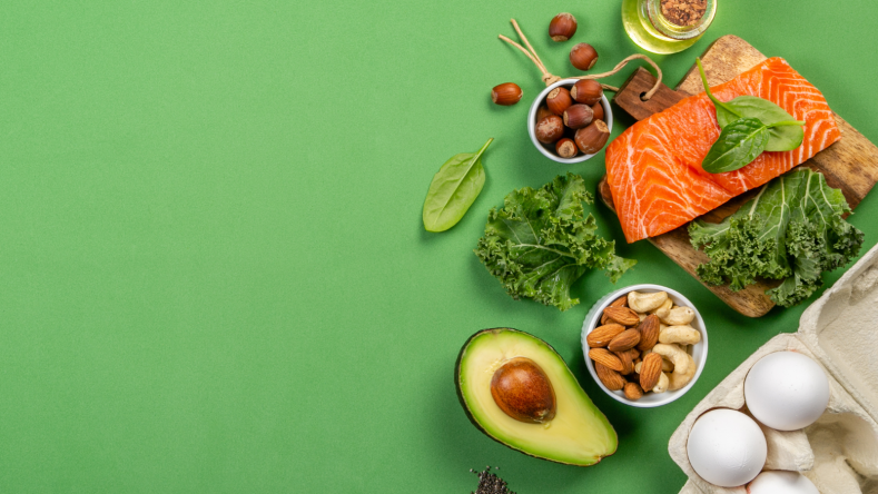 High fat foods such as salmon, nuts and avocado on a green background