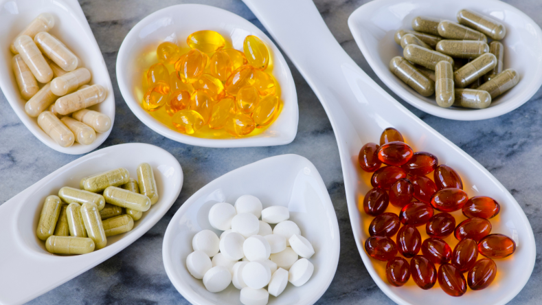 Assorted vitamins in white spoon on a marble background