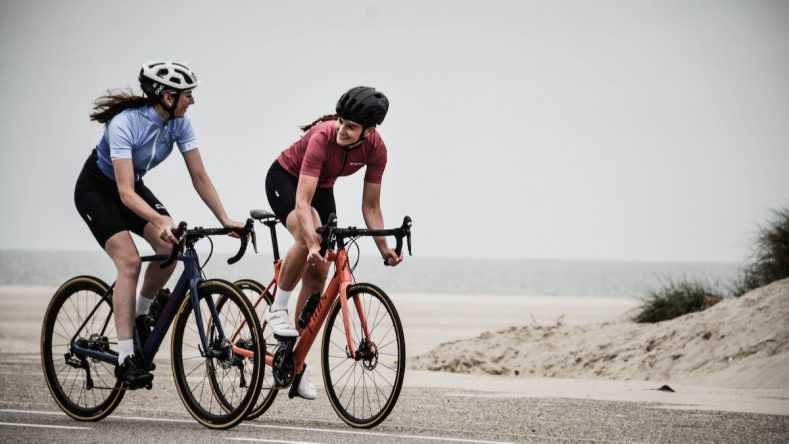 Two female cyclists cycling with a beach in the background