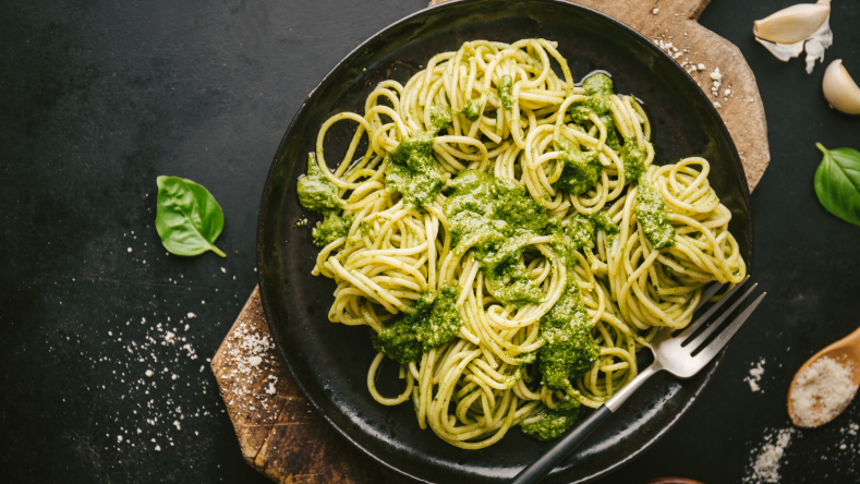 Pasta drizzled with pesto on a black plate on a dark background