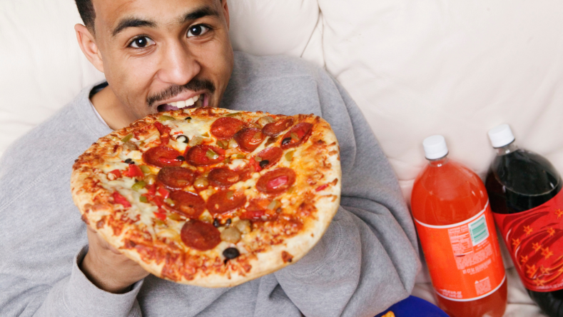 Man eating pizza with two bottles of soda in the background