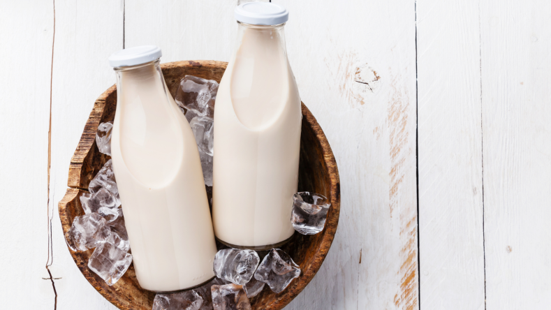 two milk bottles in a bowl of ice on a white wooden table