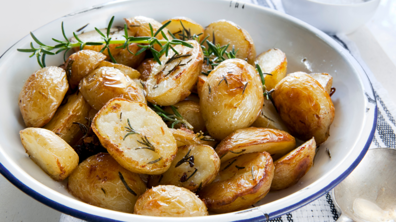 Roasted potatoes sprinkled with rosemary, in a white bowl