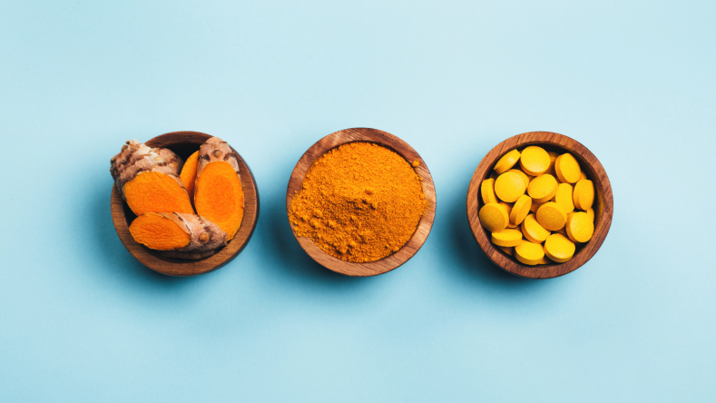 Turmeric root, powder and pills in wooden bowls on a blue background