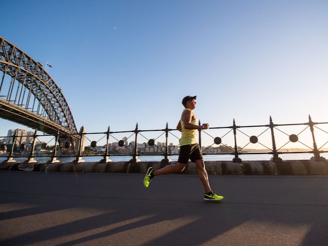 Man running in yellow sleeveless top and black shorts, with Sydney Harbour Bridge in the background