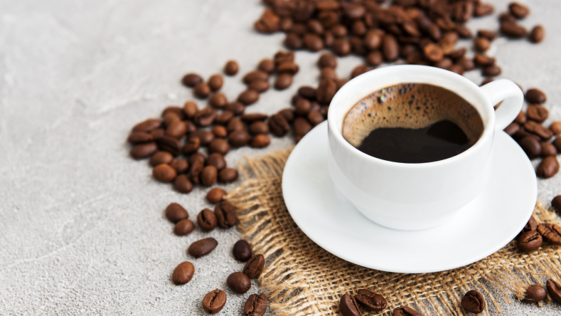 Coffee in a white cup surrounded by coffee beans on a gray background