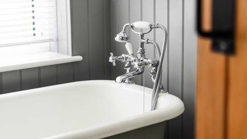 silver bath faucet and white bathtub against gray walls