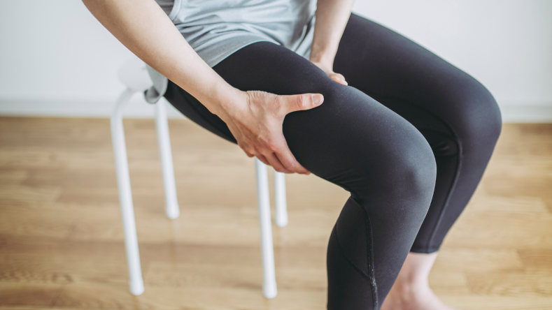 Woman in leggings grasping thigh while sitting on a white chair