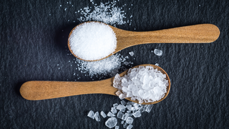 salt on two wooden spoons on a slate background