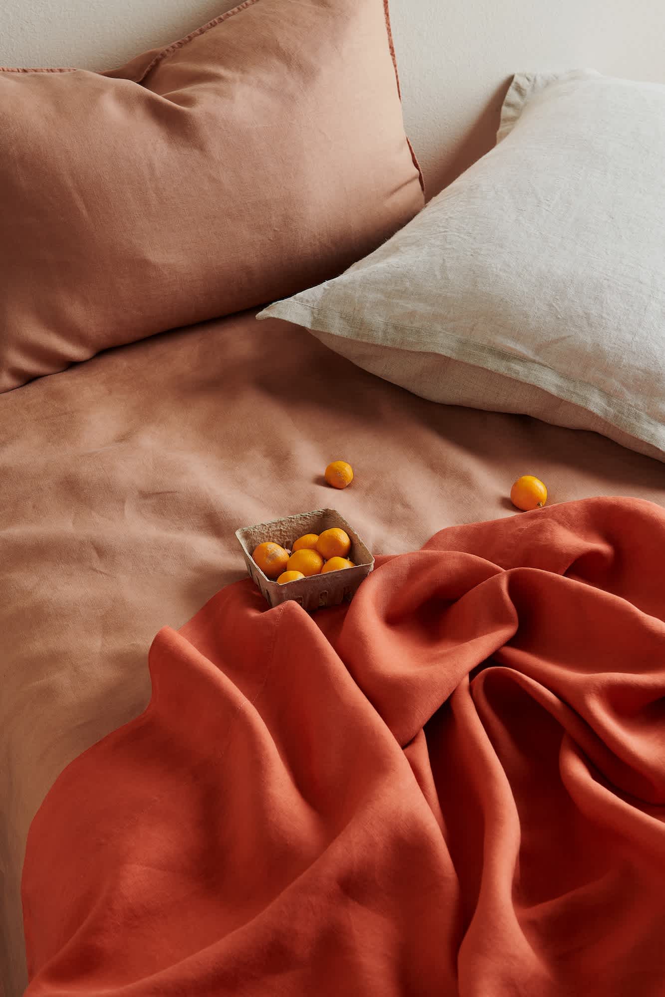 Bed with Pimento, Earth & Natural Hemp Linen bedding and a container of mandarin oranges