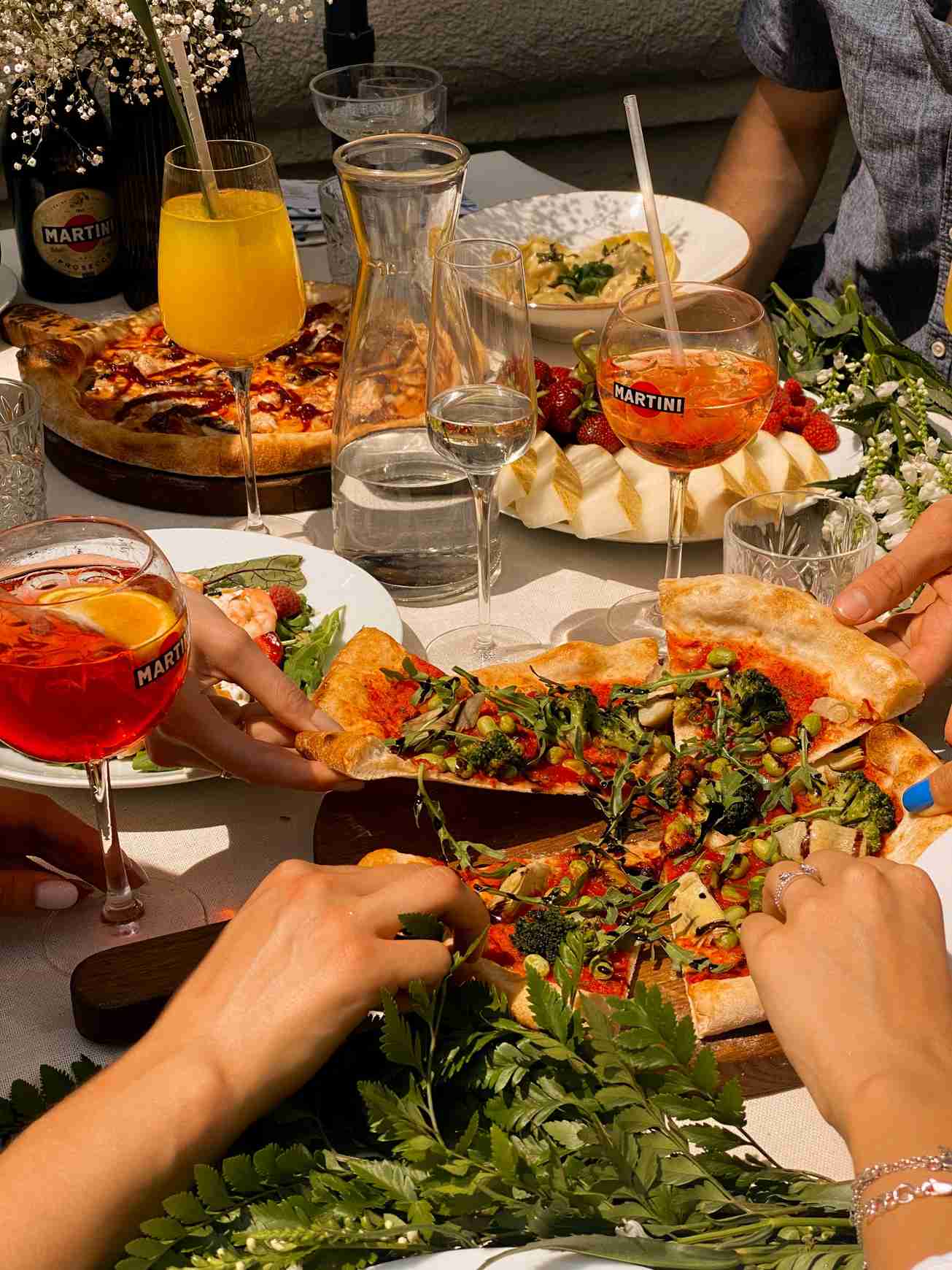 People grabbing pizza in a restaurant at a table with spritzes