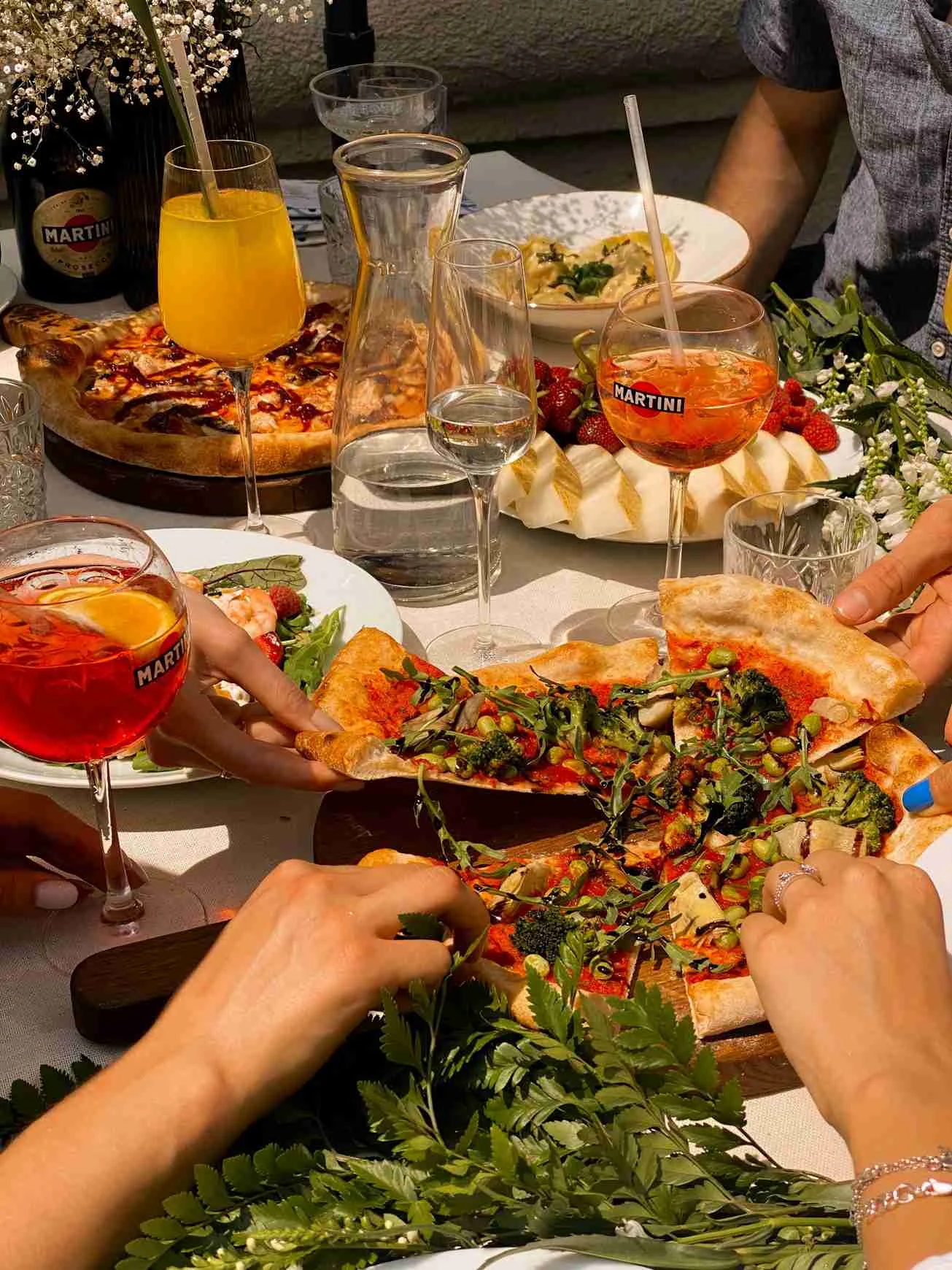 People grabbing pizza in a restaurant at a table with spritzes