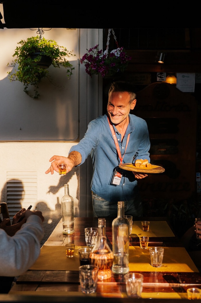 A man holds a tray of food and passes out samples to people at a dinner table in Florence.