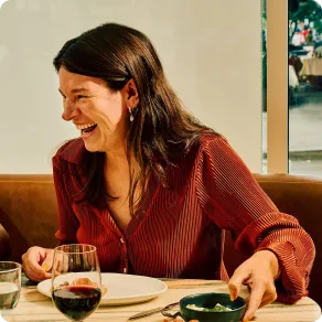 Woman laughs seated at a table with a glass of red wine