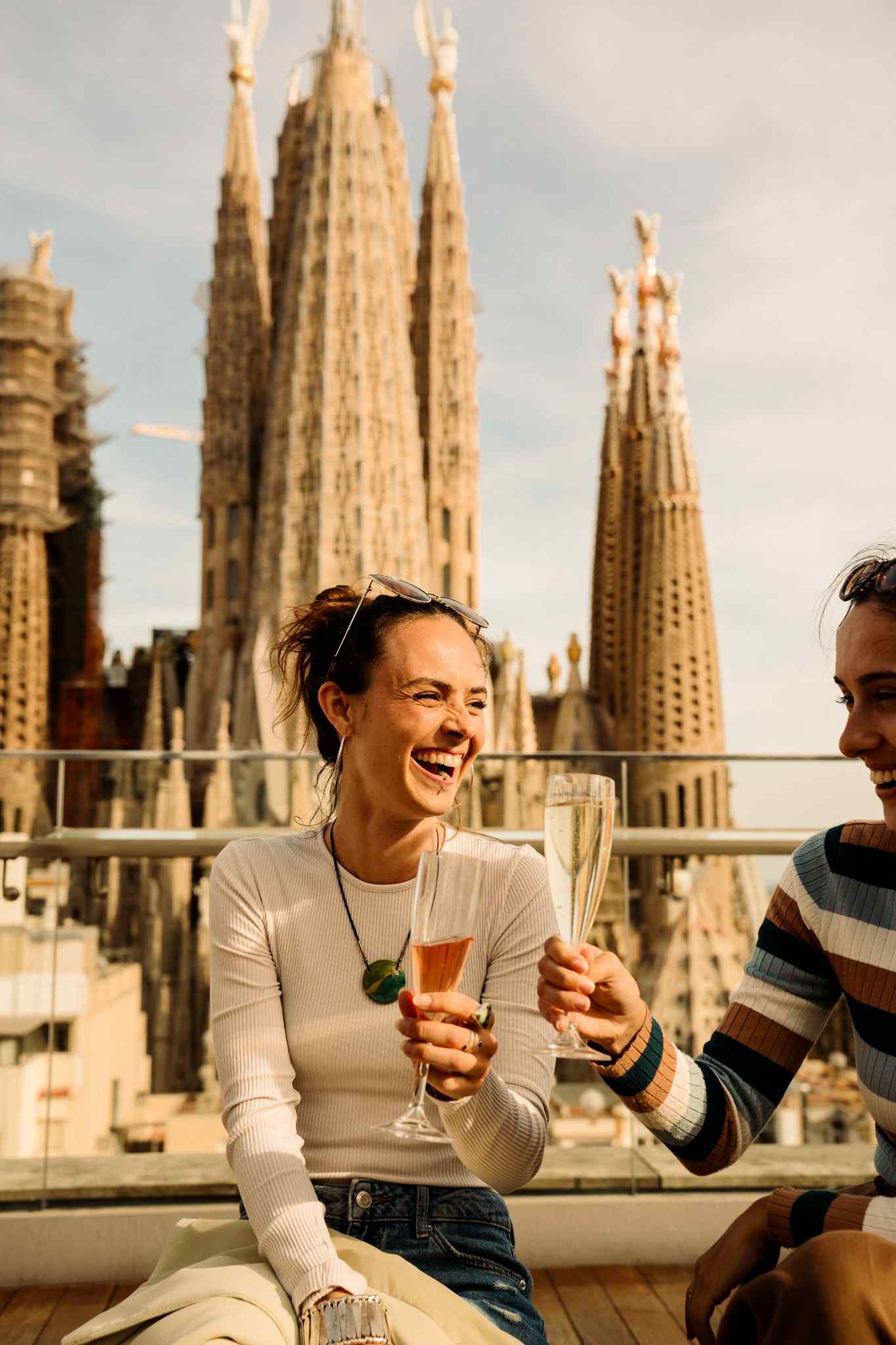 Woman drinking a class of cava on rooftop in Barcelona with Sagrada Familia in background