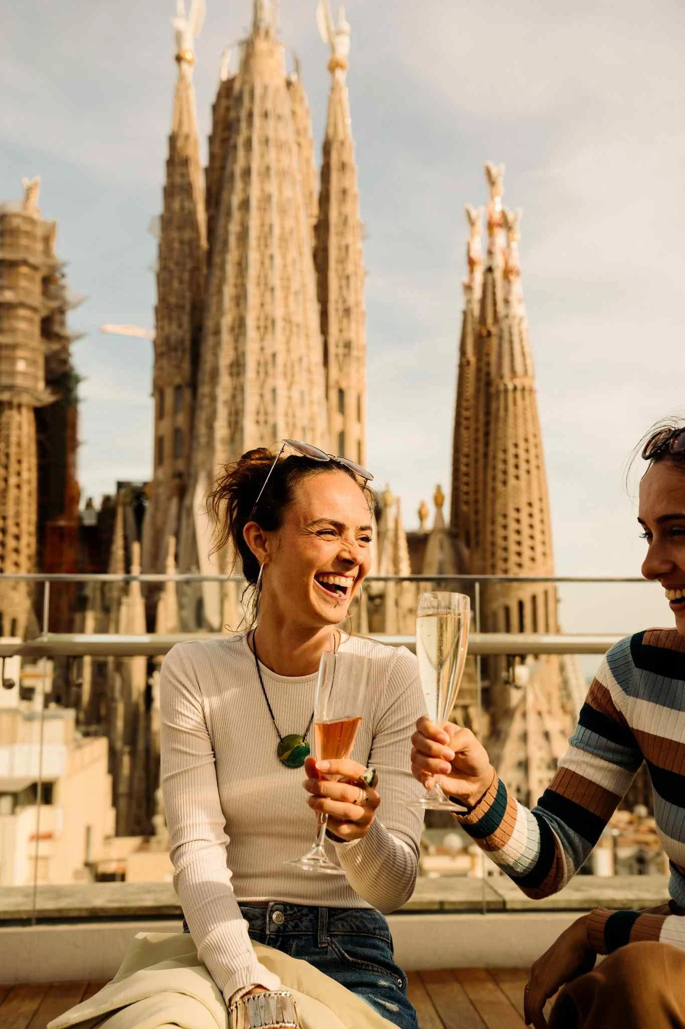 Woman drinking a class of cava on rooftop in Barcelona with Sagrada Familia in background