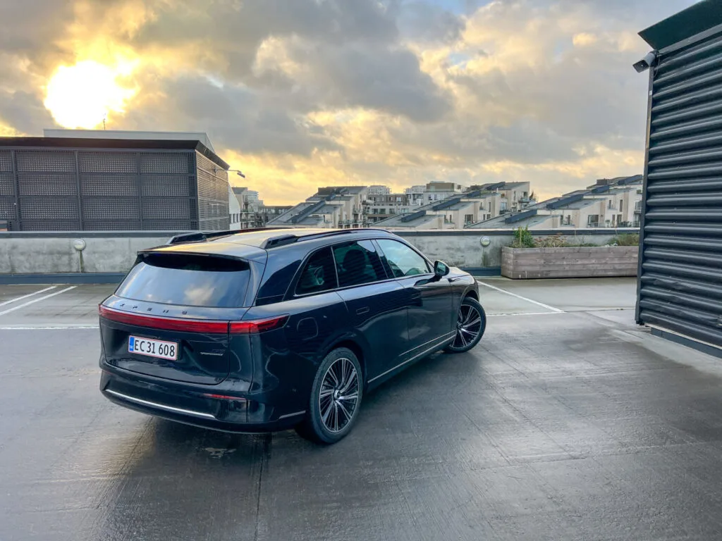 Baksidan av mörk XPeng G9 på parkering med utsikt över stad i skymning