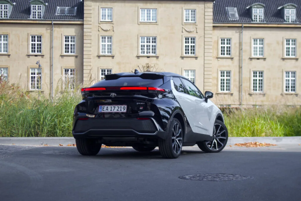 Mörk Toyota C-HR sedd bakifrån, parkerad framför husfasad