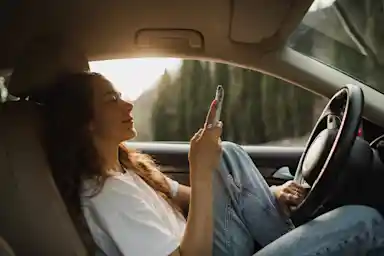Kvinna i förarsätet av bil tittar på mobil