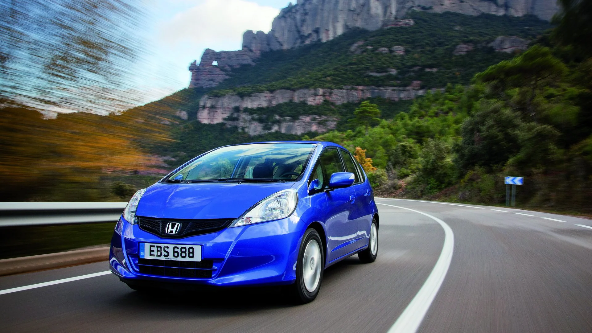 Blå Honda Jazz fotad framifrån på väg bland bergen