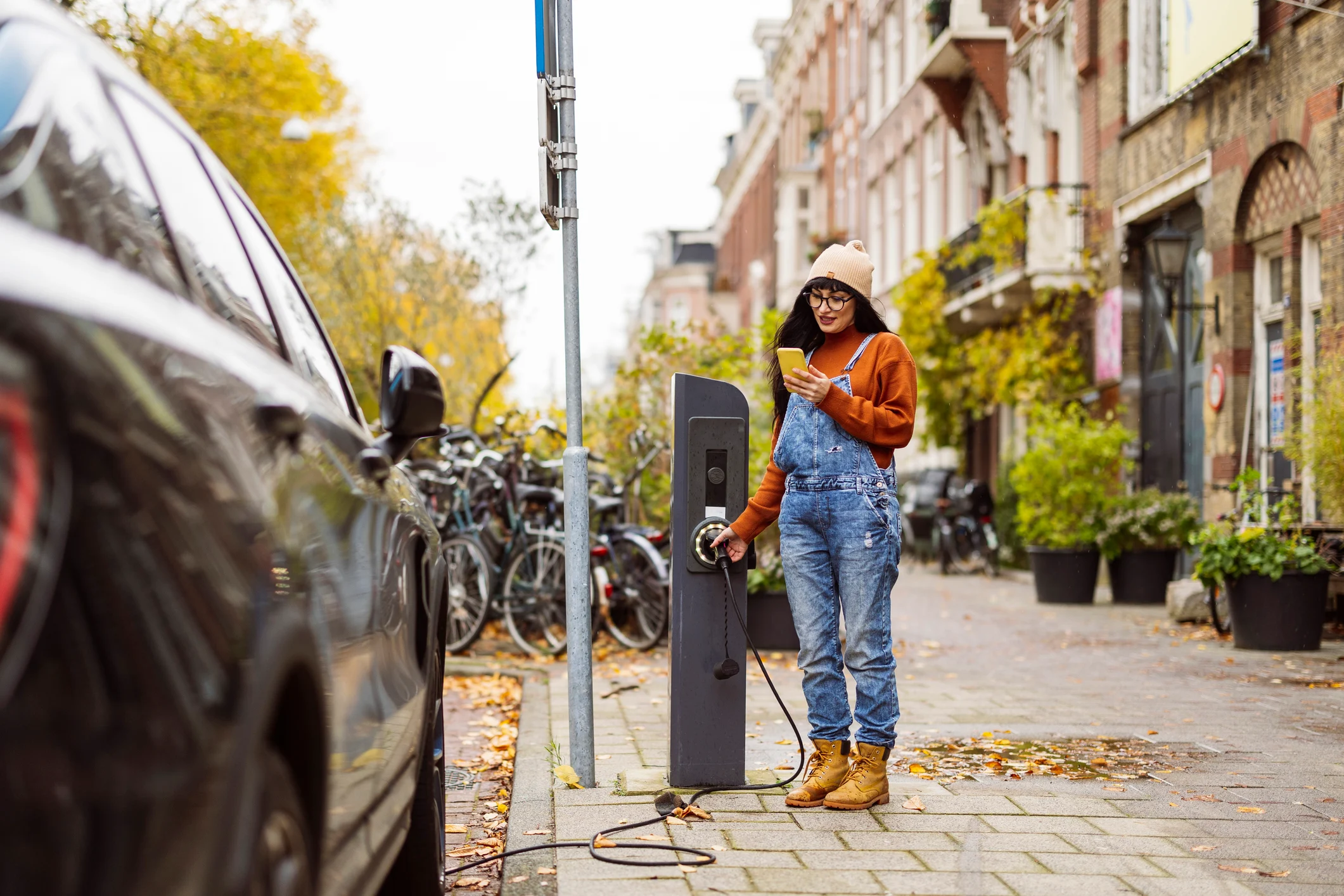 Svart elbil laddas av kvinna på gata.