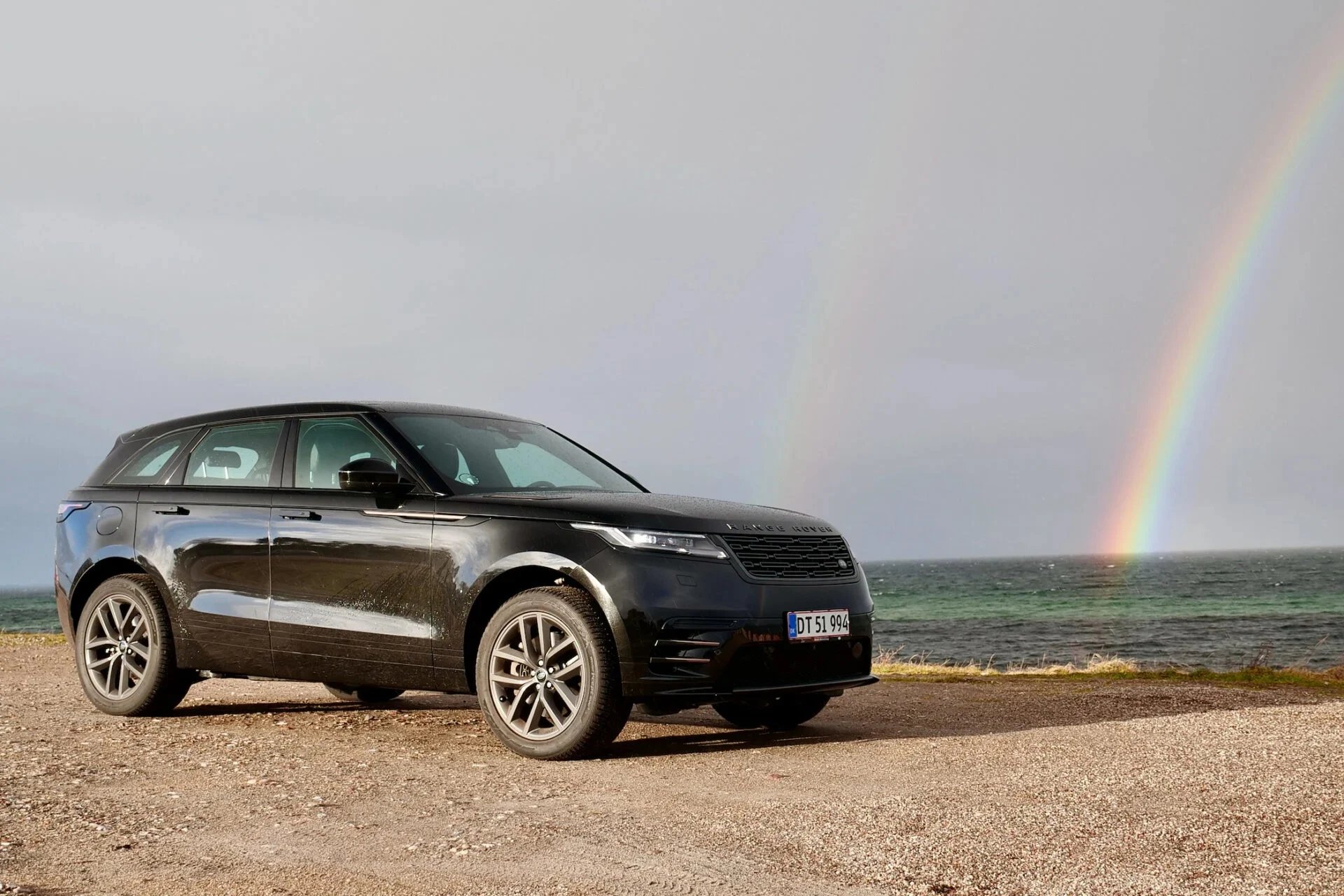 Svart range rover på strand framför regnbåge
